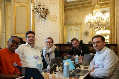 Photo des 5 membres de l'équipe lors du hackathon autour d'une table avec leurs ordinateurs dans un salon du ministère